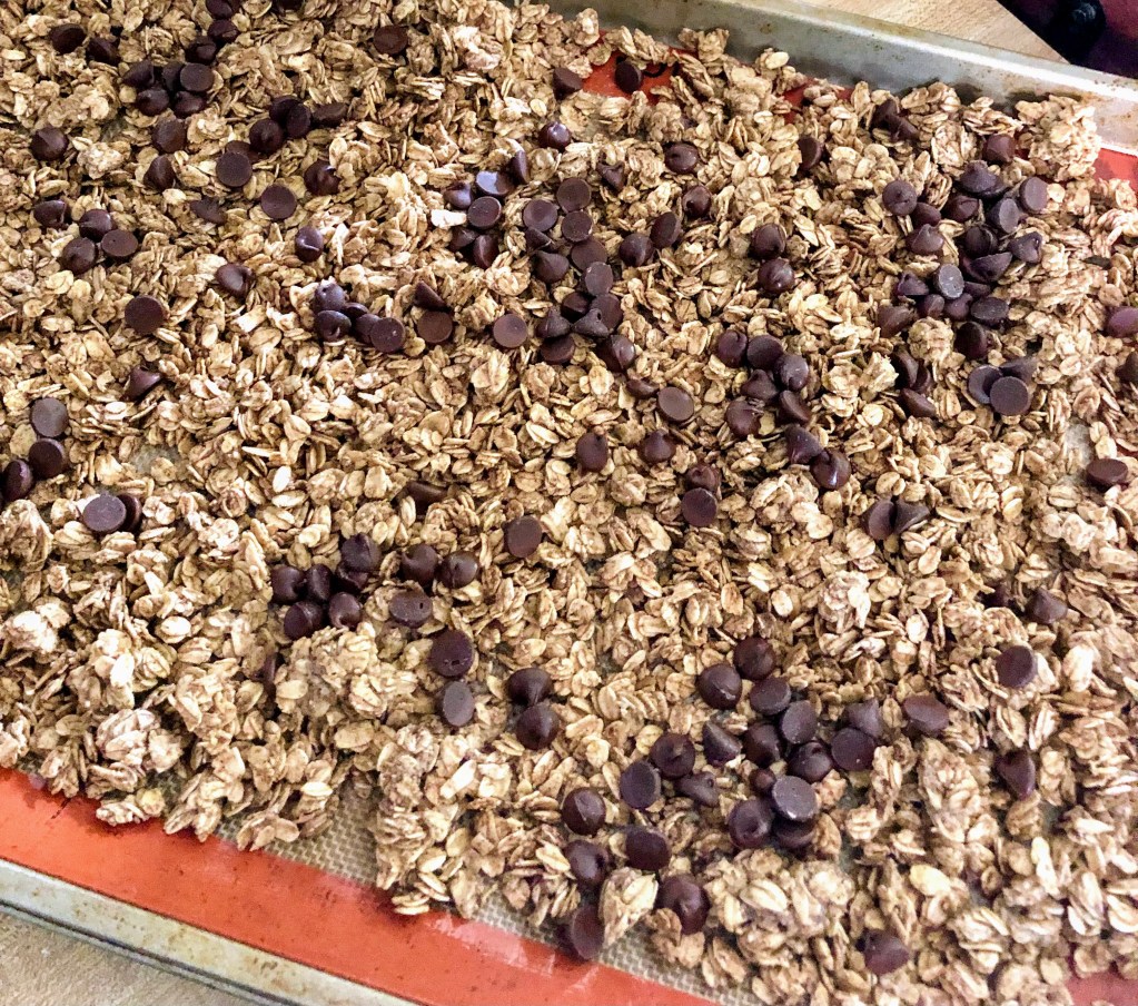 A cookie sheet is filled with heart healthy, whole grain granola and chocolate chips, fresh from the oven.