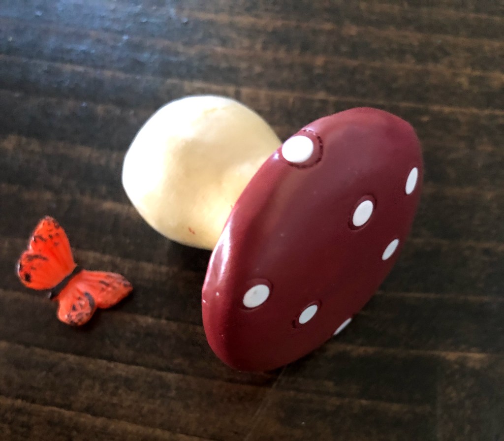 A small mushroom figurine lays next to a butterfly.