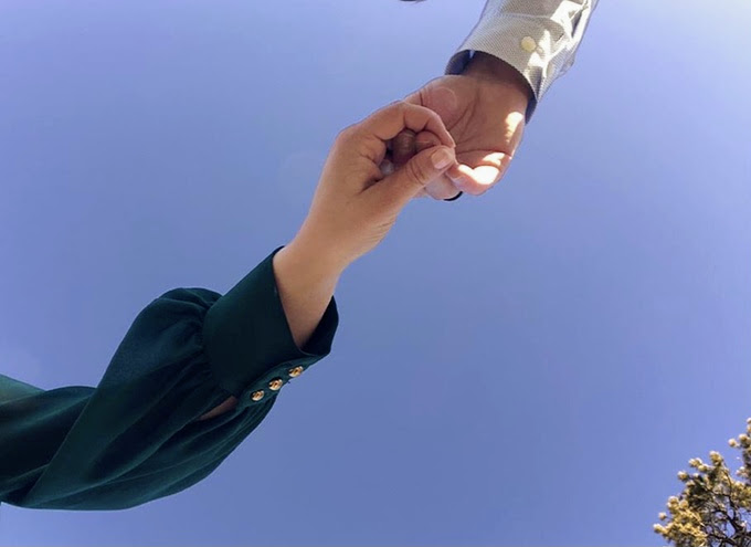 A man and woman hold hands, with the bright blue sky above them.