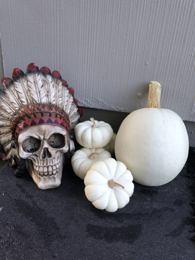 A skull sits near white pumpkins on a door stoop.