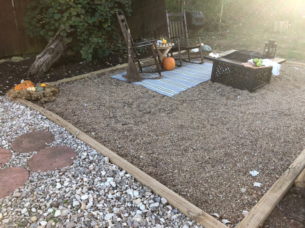 A cottage-style pea gravel patio has been decorated for the autumn season with pumpkins and such.