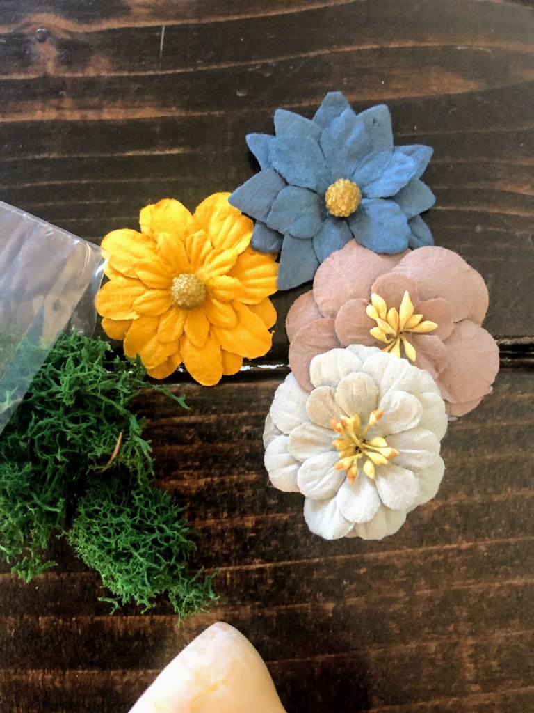 Faux flowers lay on a kitchen table, waiting to be used on making a fairy lantern.