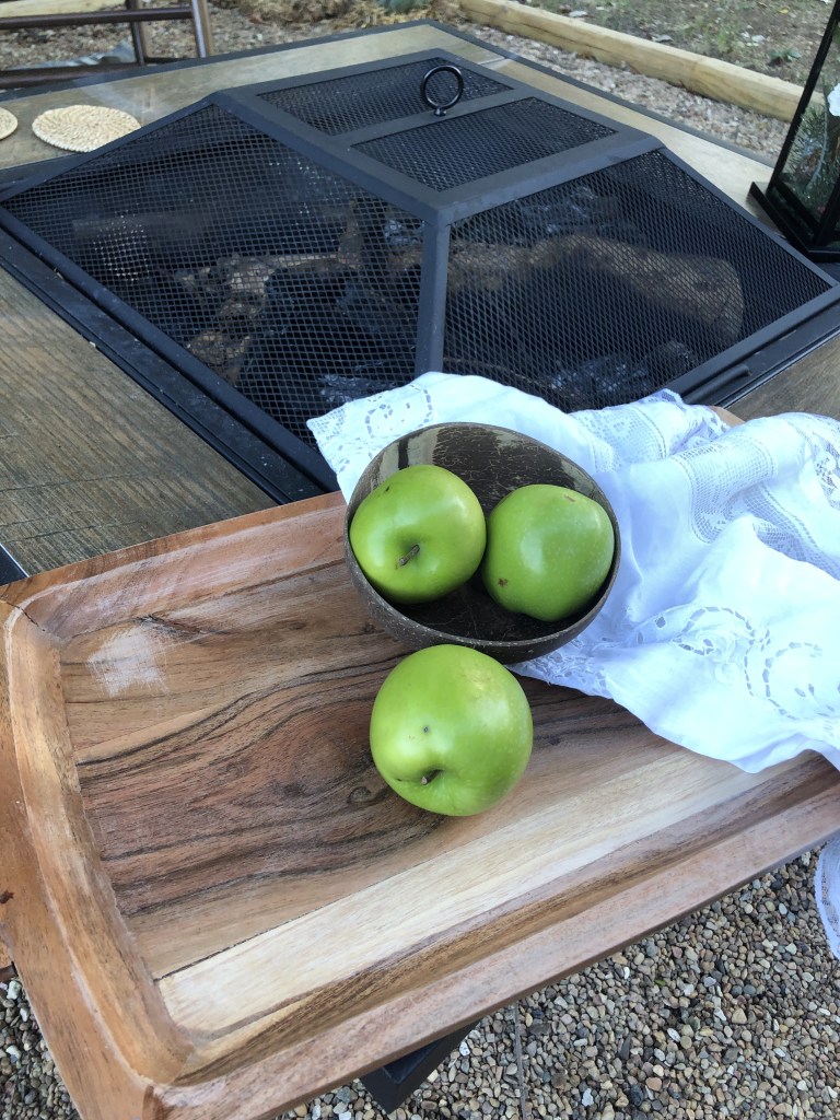 Green apples sit on a wood tray on fire pit.