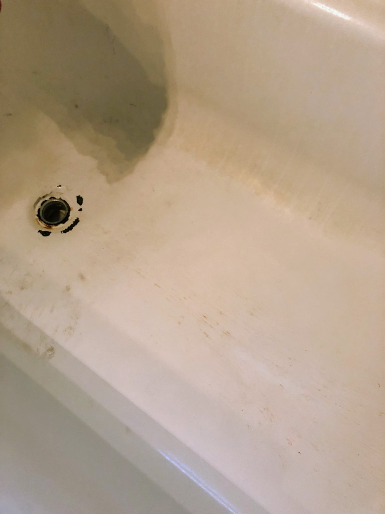 An old bathtub has grime and rust on it before being refinished.