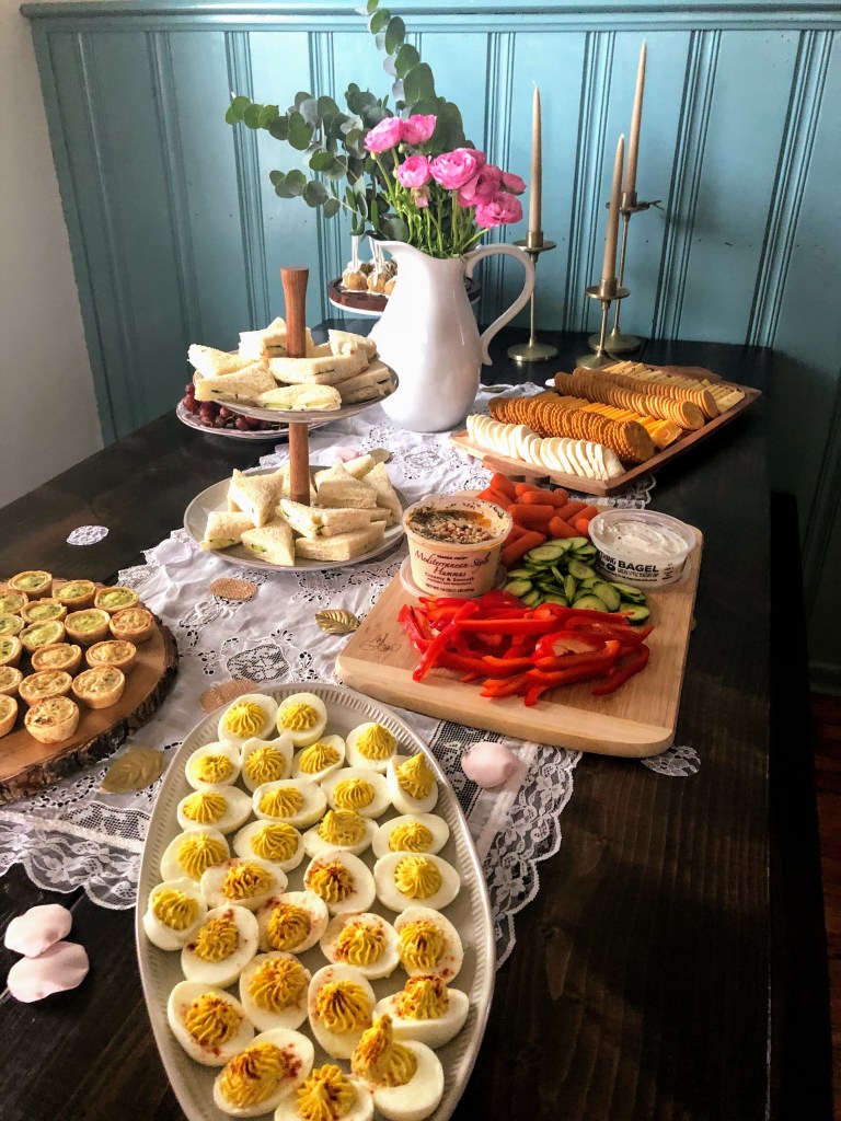 An antique table runner sits under a display of appetizers and a pitcher of flowers in a cottage-style dining room as inspiration to decorate with antiques.