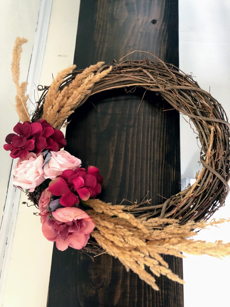 A bench has a wreath laid on it with wheatgrass and flowers.