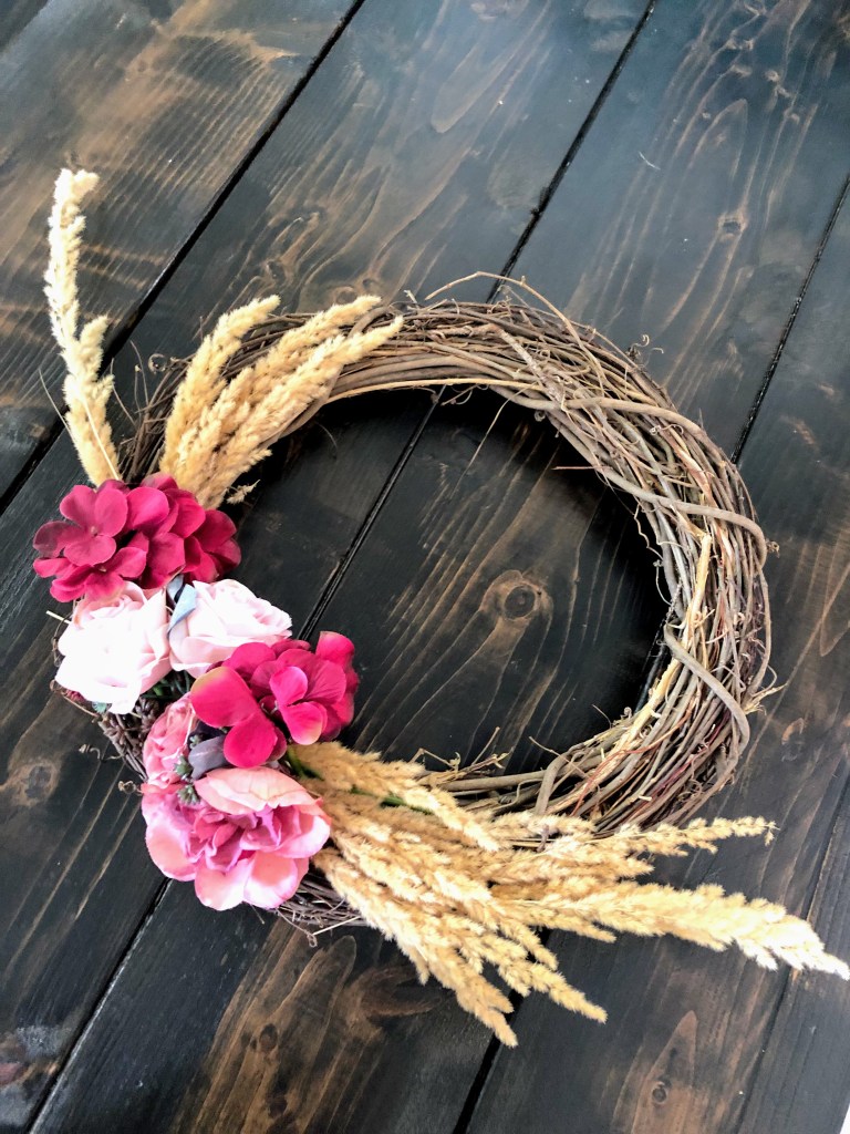 A purple and light pink floral wreath with wheatgrass in it.