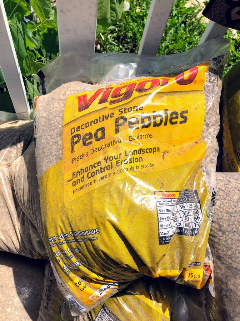 A large pile of pea gravel lays against a white picket fence.