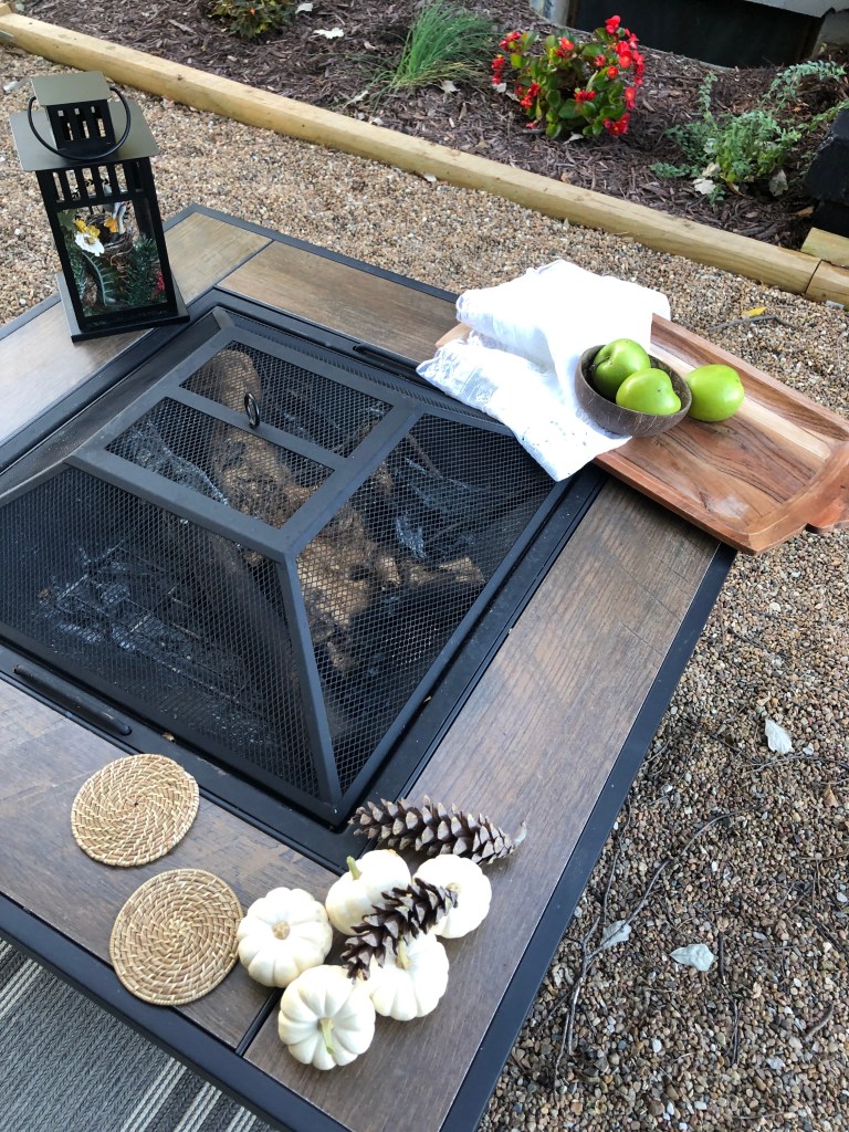 A fire pit sits with various items on a fall pea gravel patio.
