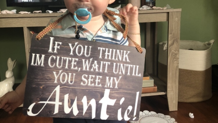 A young boy wears a sign that says, “If you think I’m cute, wait until you see my Auntie.” 