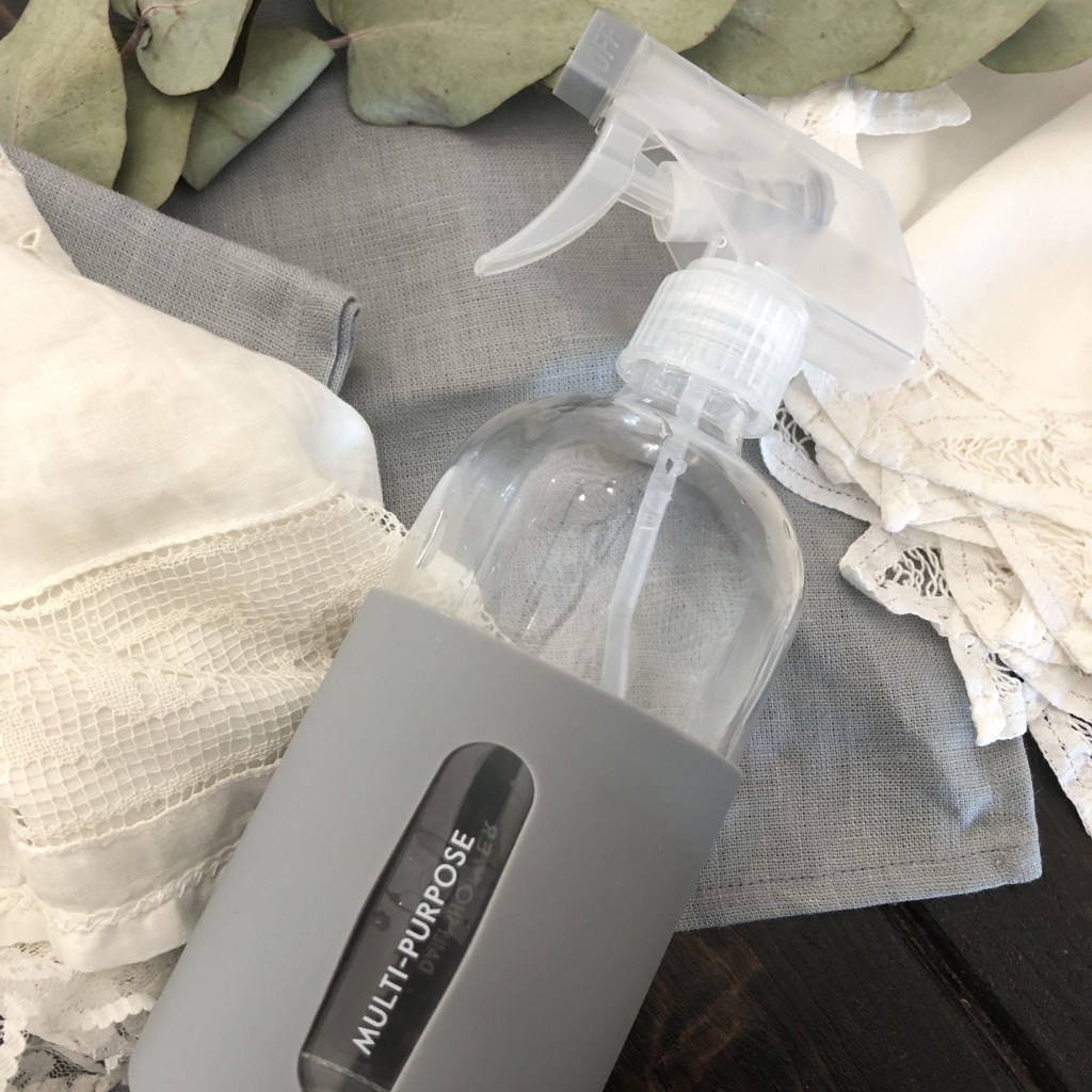 Natural cleaning with vinegar water in a reusable spray bottle, spread out on a table alongside some foliage and linens. 