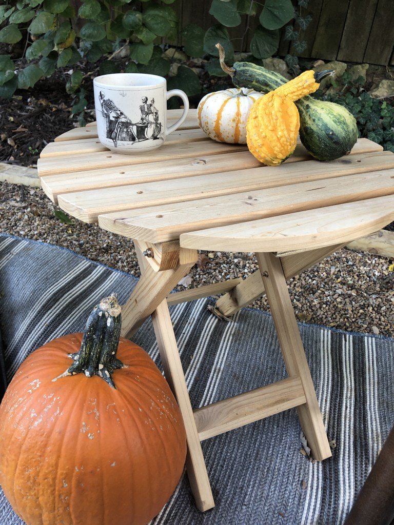 Gourds sit on a small side table on a pea gravel patio outside. 