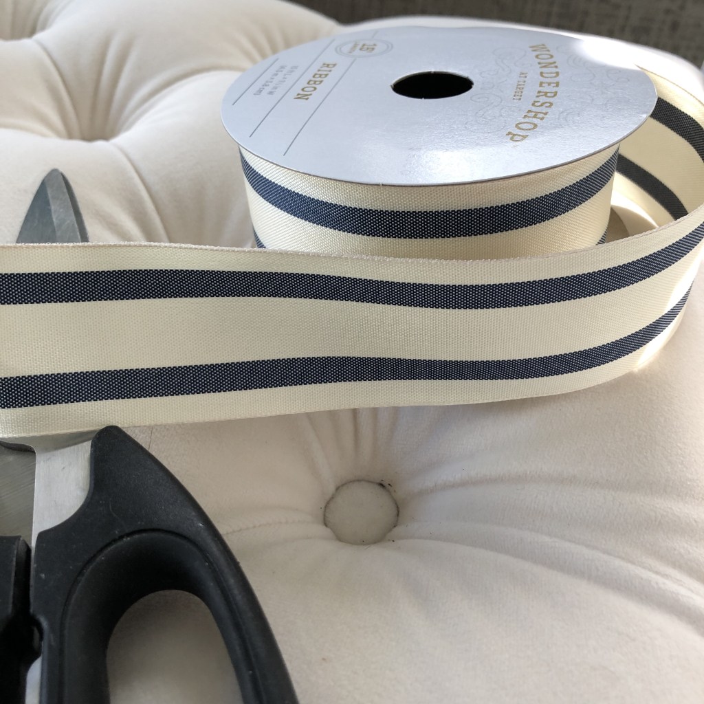 White with blue stripes, a ribbon lays on a white bench, ready to be put on a Scandinavian holiday tree.