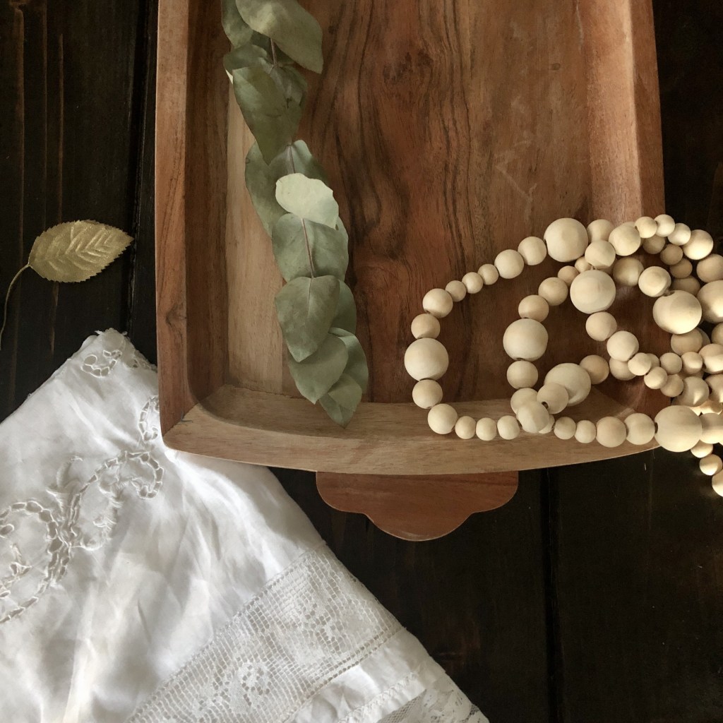 Many items such as faux gold leaves, wooden beaded garland, eucalyptus, and linens will be used for making a Thanksgiving tablescape.