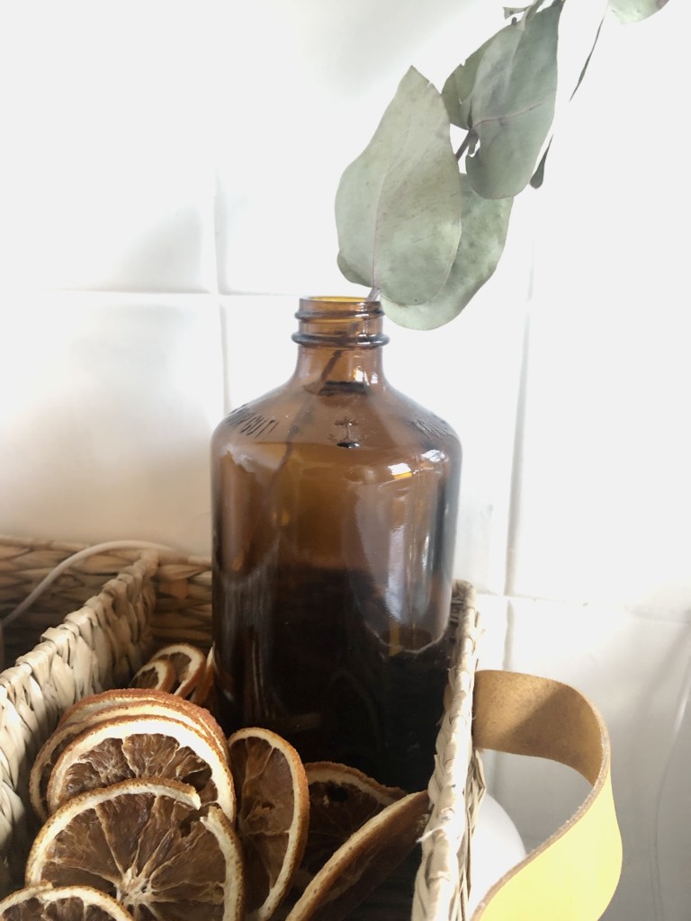 Dried, sliced citrus is placed around an amber vase with a single eucalyptus branch in it for the inter season.