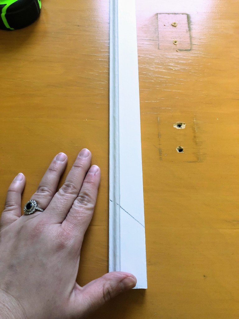 A woman places her hand next to white moulding to measure it for learning how to make an old door look new.