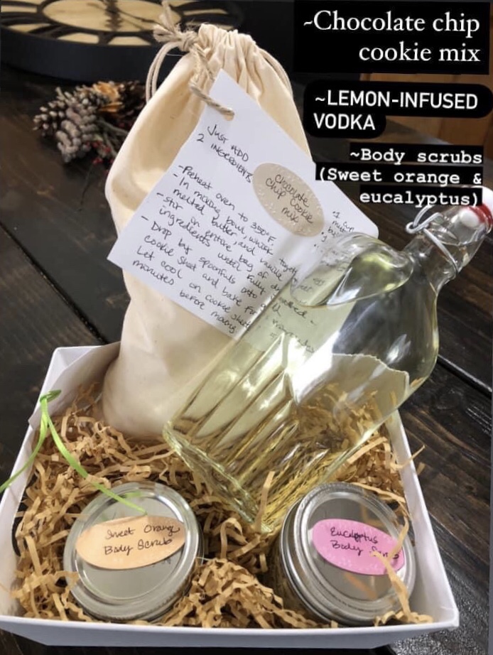 DIY gift baskets consisting of sugar scrubs, cookie mix, and lemon-infused vodka sit on a dining table. 