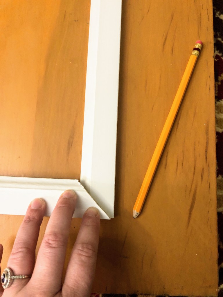 A woman places corners together to fit moulding together on a door for a DIY interior door makeover.