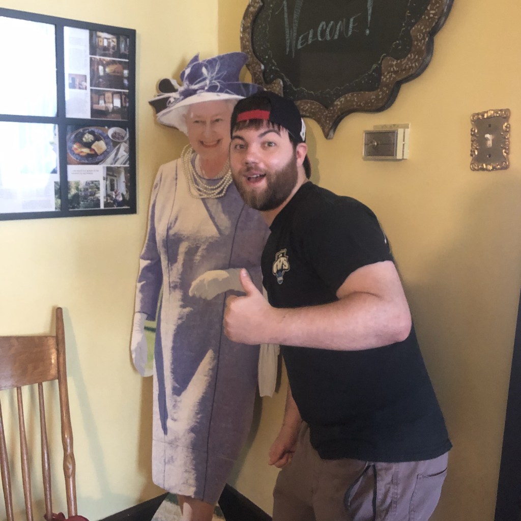 A man poses next to a cardboard cutout of the Queen of England.