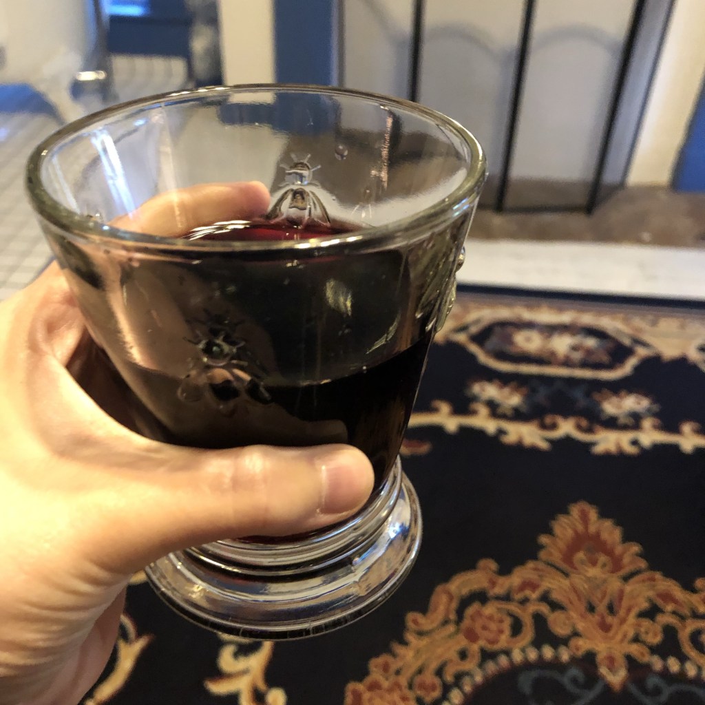 Red wine is being held with a Victorian rug, fireplace, and clawfoot tub in the background.