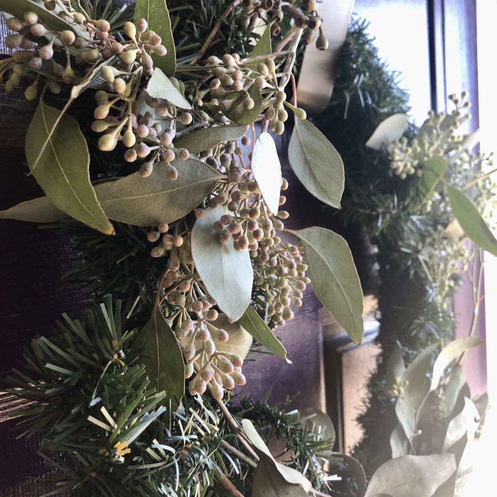A homemade wreath has been wrapped with eucalyptus branches and hanging on a deep purple front door.