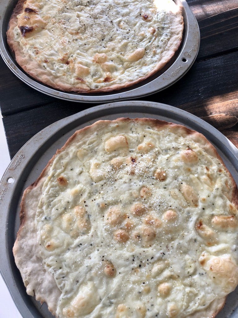 Two white pizzas are baked and ready to be eaten for dinner.