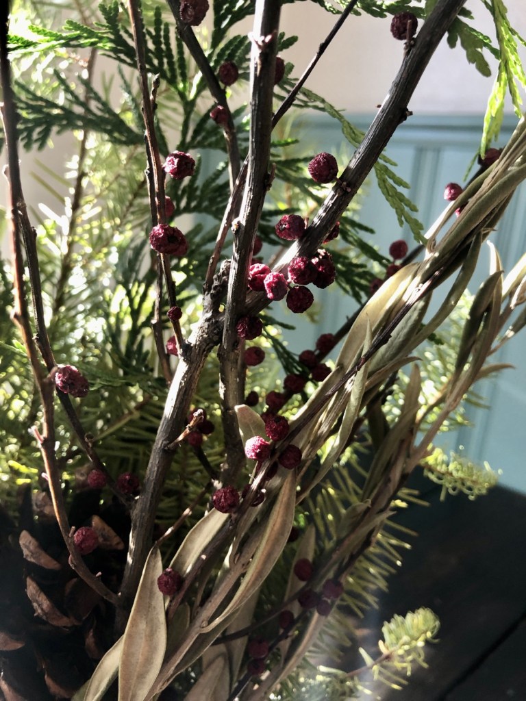 Winter foliage has been placed in a porcelain vase on a table, with lots of natural light shining in on it. 