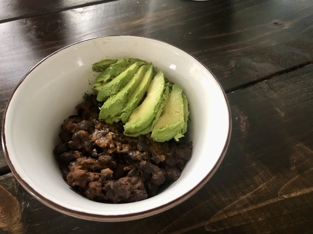 A heart vegetarian chili is bowled with chopped avocado and corn tortillas.