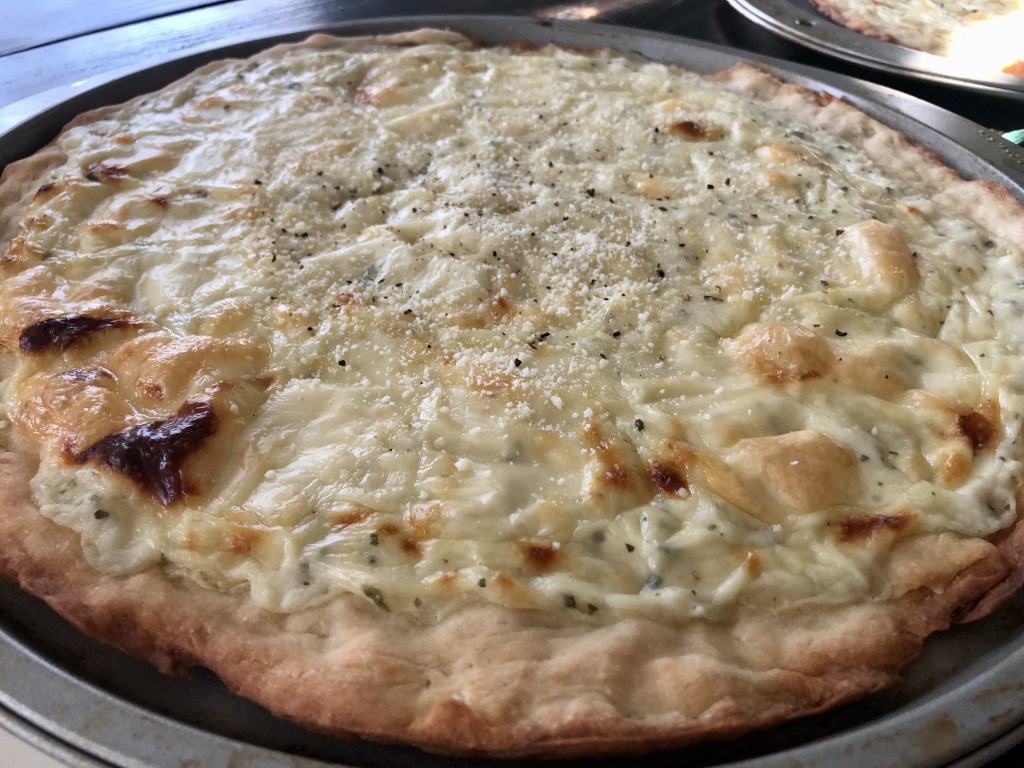 Alfredo white pizza recipe sits on a kitchen table, with natural daylight streaming in.