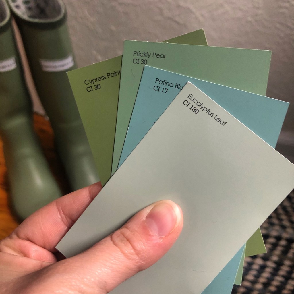 A palette of paint colors is held up with gardening boots behind. This display is used as a demonstration for the best painting tips for beginners.