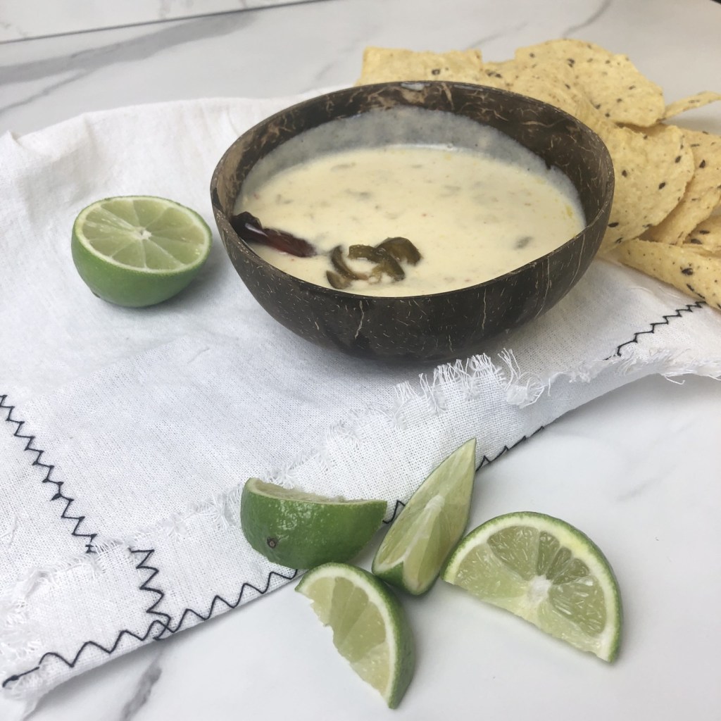 Super Bowl Queso sits on a linen on a marble tabletop with limes nearby.