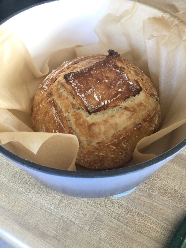 Freshly baked easy artisan bread sits on parchment paper inside a dutch oven that has just been removed from the oven.