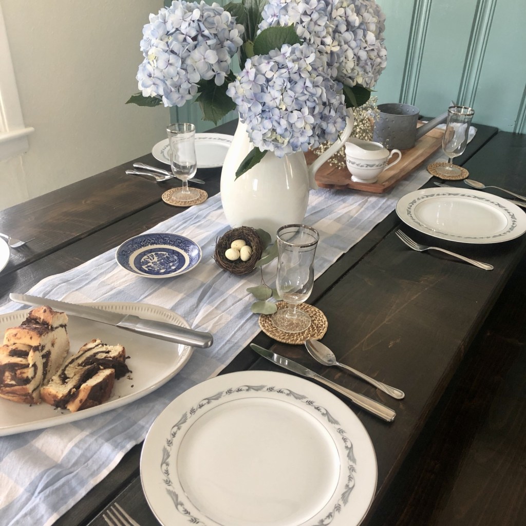 Spring table decor is spread out over a long dining table with lots of fresh flowers and other springlike pieces for a cottage.