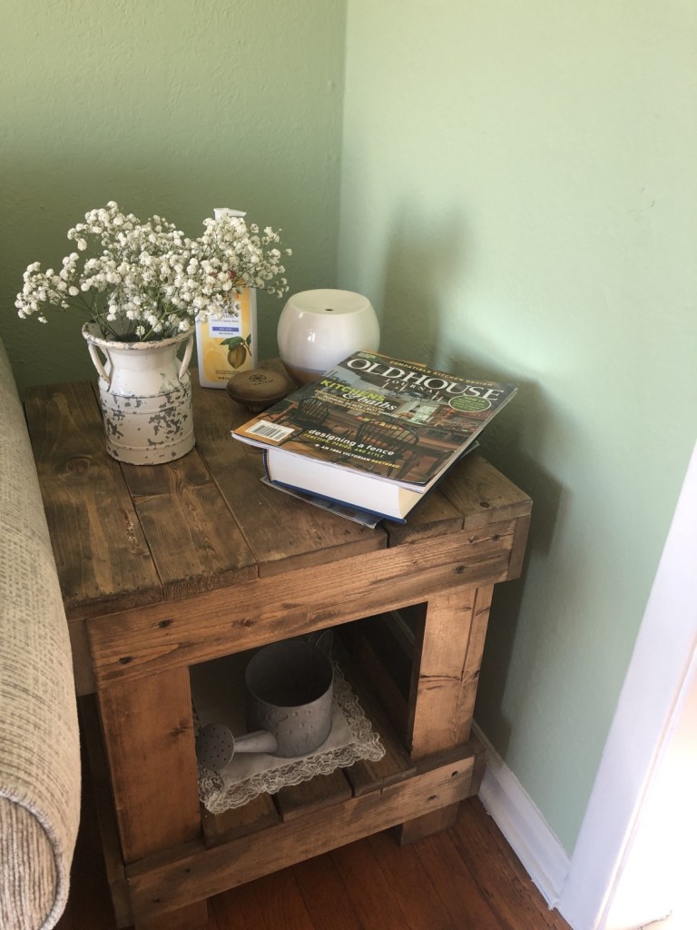 Fresh baby's breath sits in a rustic vase on a side table in a living room for spring.