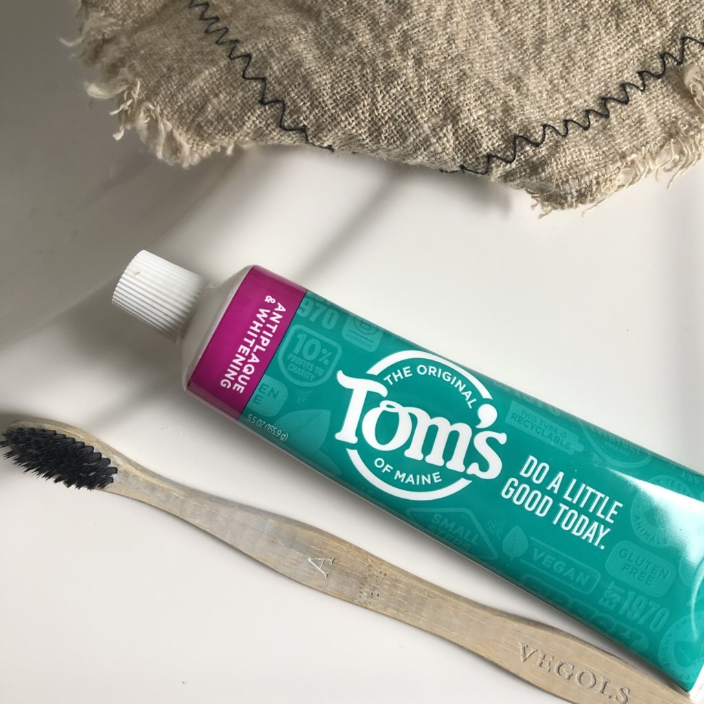 Tom's toothpaste lays with a bamboo toothbrush near a bathroom sink.