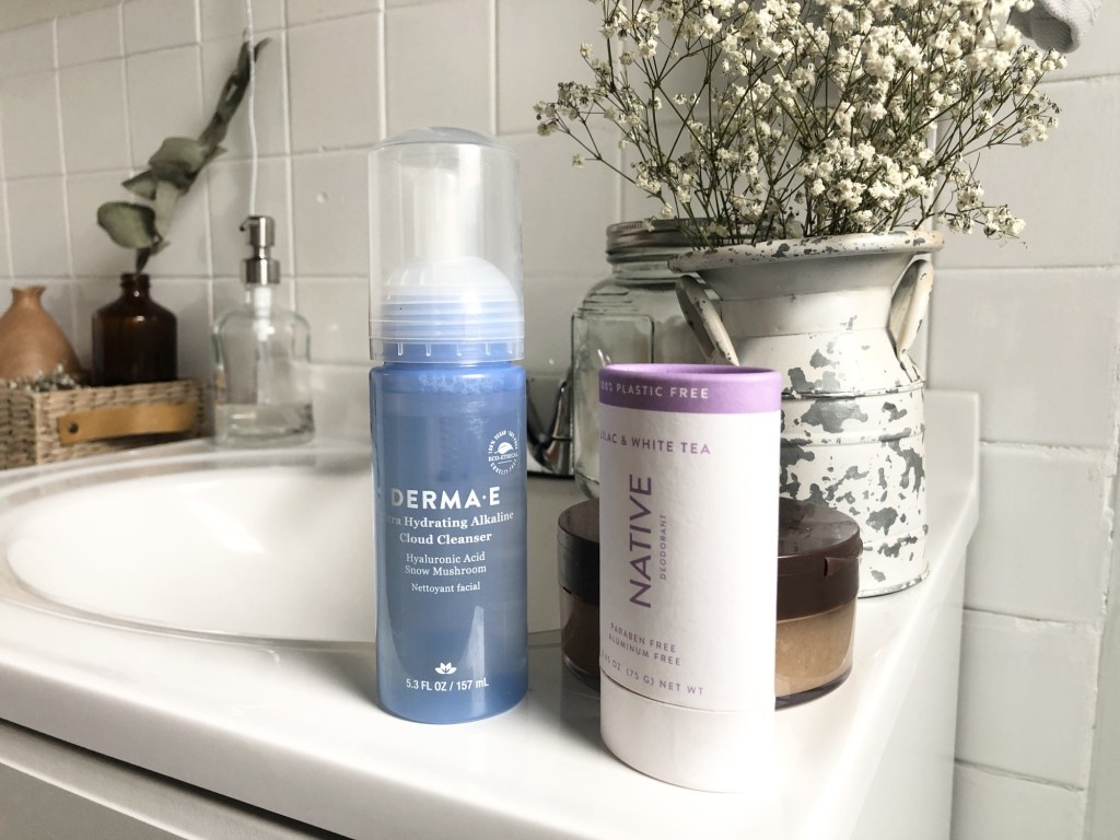 Several beauty products await in a bathroom as flowers sit on the counter behind them.