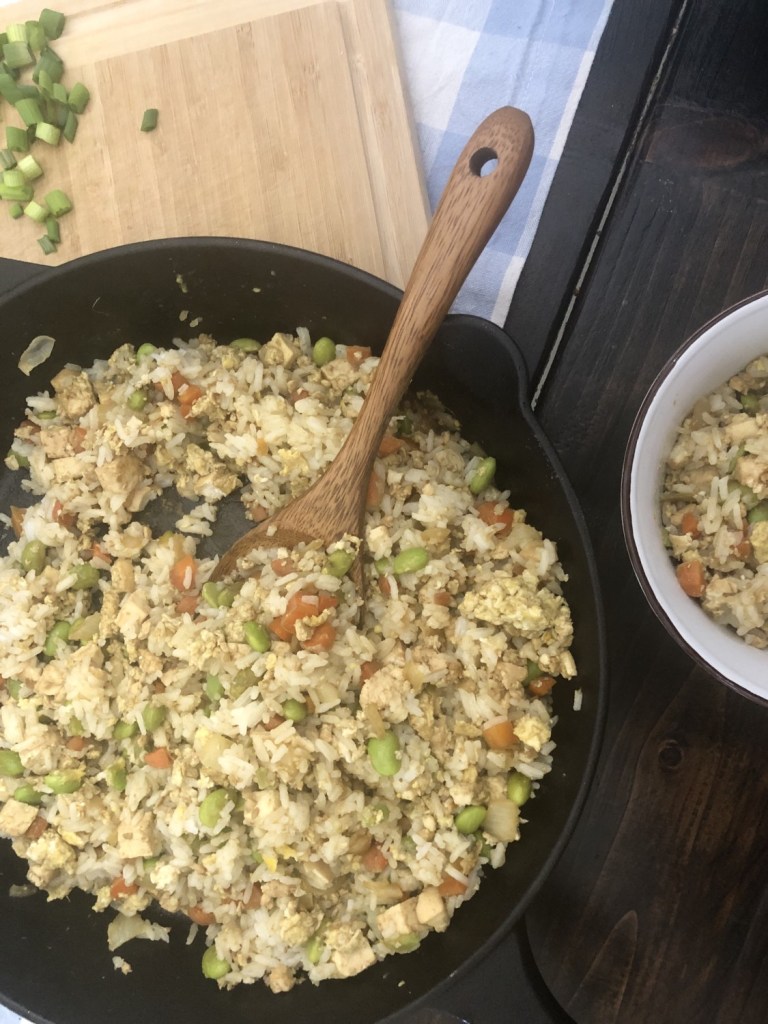 Vegetarian fried rice sits in a skillet on a table with sliced green onions on the side to garnish it.