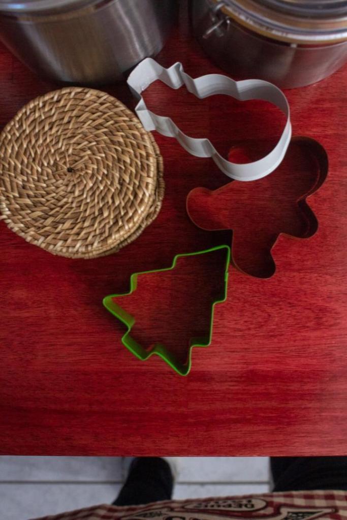 Cookie cutters lay on a red table for some cookie decorating as part of a Christmas brunch entertaining idea.