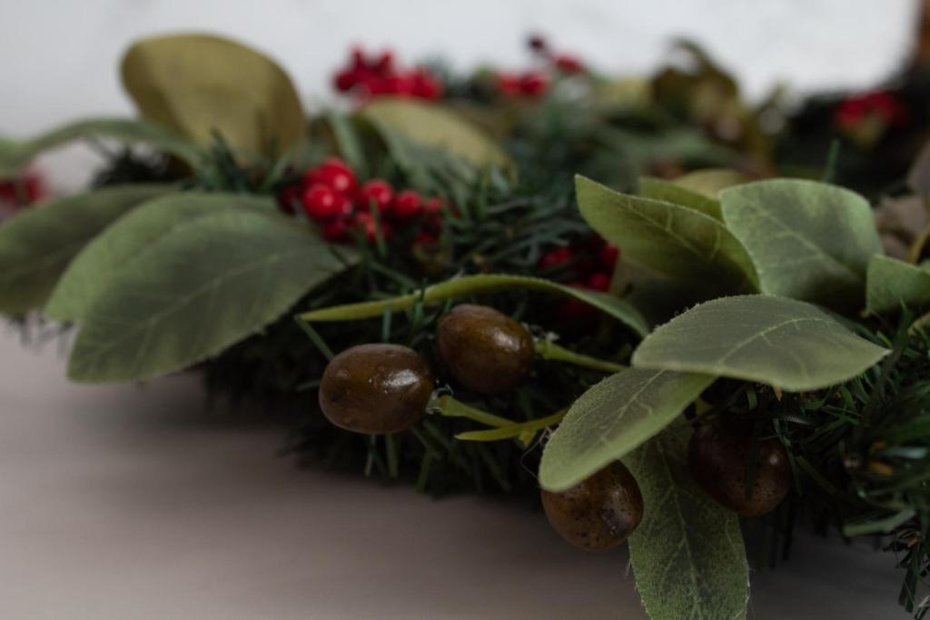 A close-up of a wreath that is decorated in olive branches, eucalyptus, and bright berries is laid out.