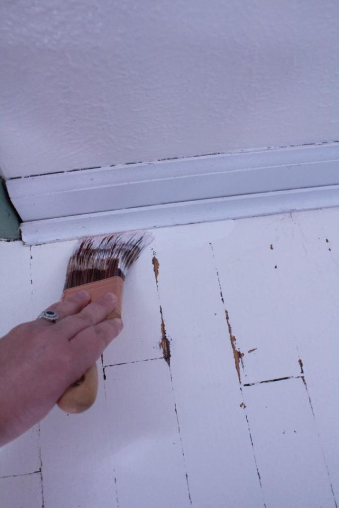 A woman is cutting in around baseboards using an angle brush land white paint.