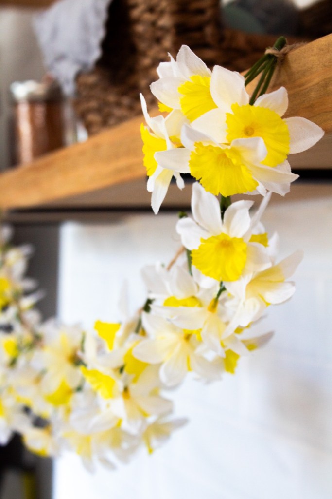 A DIY daffodil garland is strung on an open shelf above a stove.