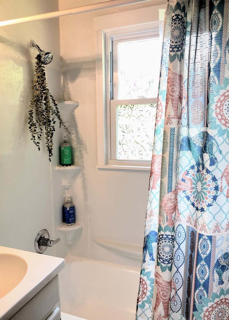 A newly refinished bathtub has eucalyptus hanging from the shower head and a window with morning light coming in.
