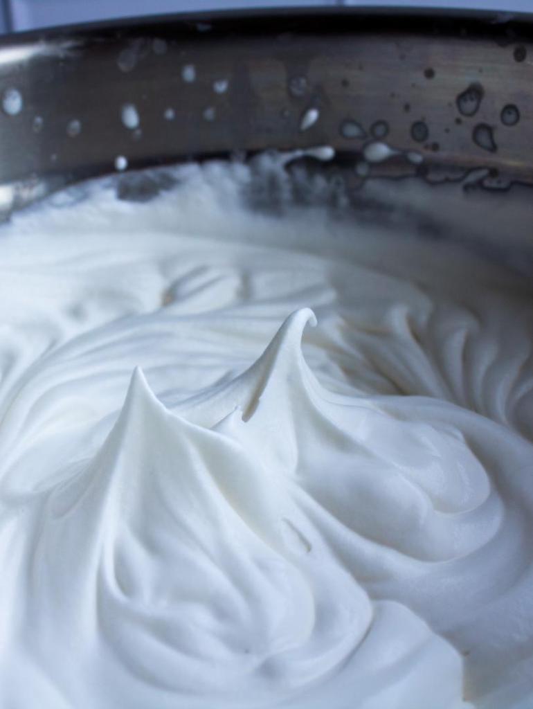 An up-close shot is shown of whipped cream in a stainless steel bowl, with its gentle peaks.