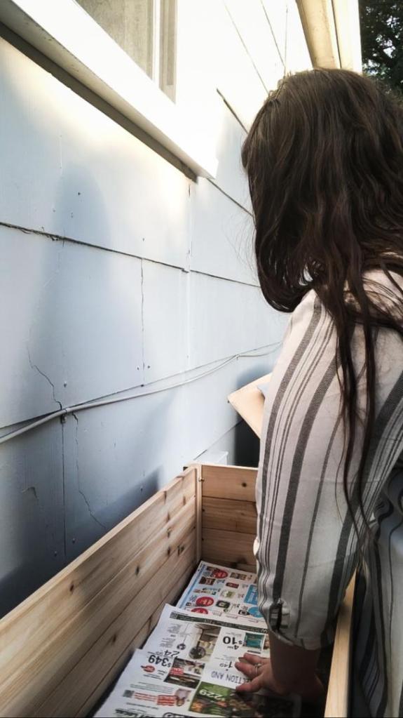 A woman lays newspaper down into a raised bed.