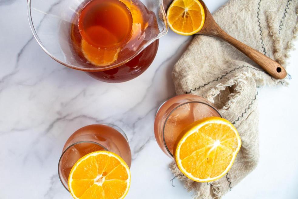 A virgin sangria mocktail is poured into glasses and a pitcher and garnished with orange slices.