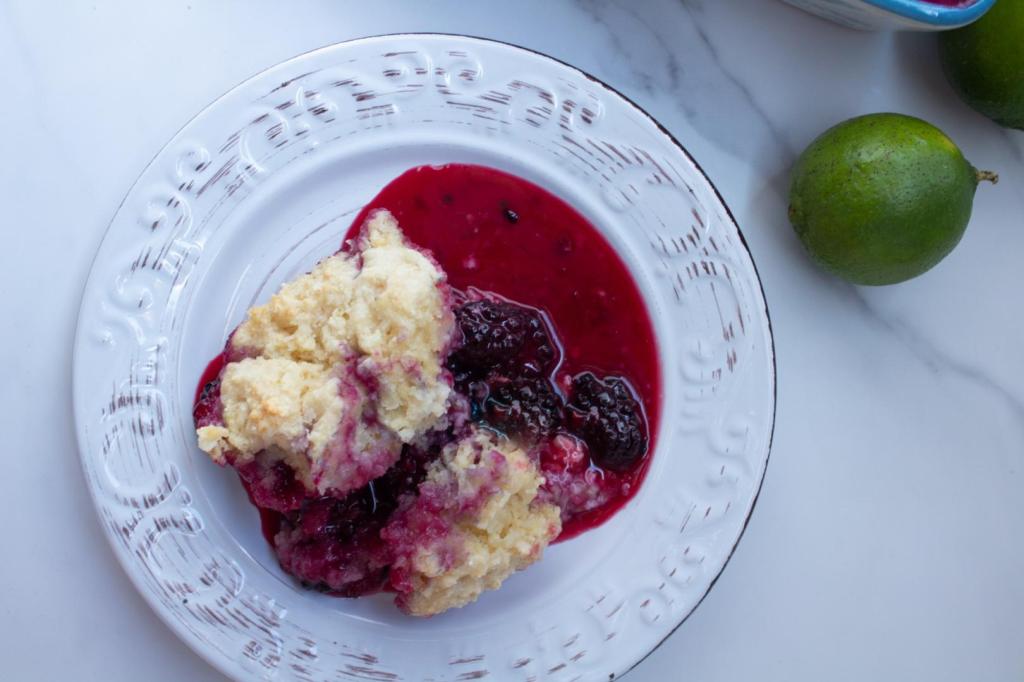 Blackberry cobbler has a sauce oozing from the cobbler with limes arrange alongside it.