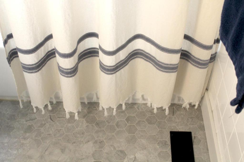 A shower curtain hangs beautifully toward the marbled tile floors.