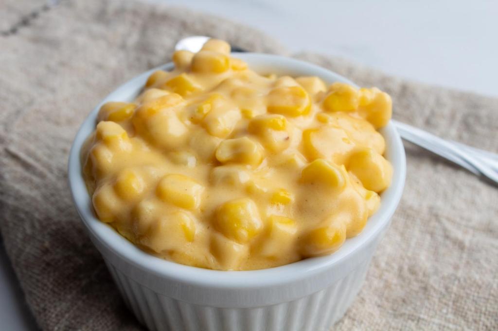 Cheesy corn is presented in a white ramekin alongside a spoon.
