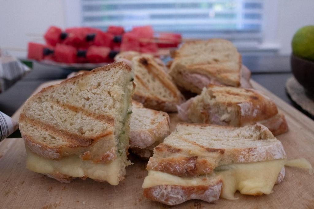 Delicious grilled paninis sit in front of fruit skewers on a dinner table.