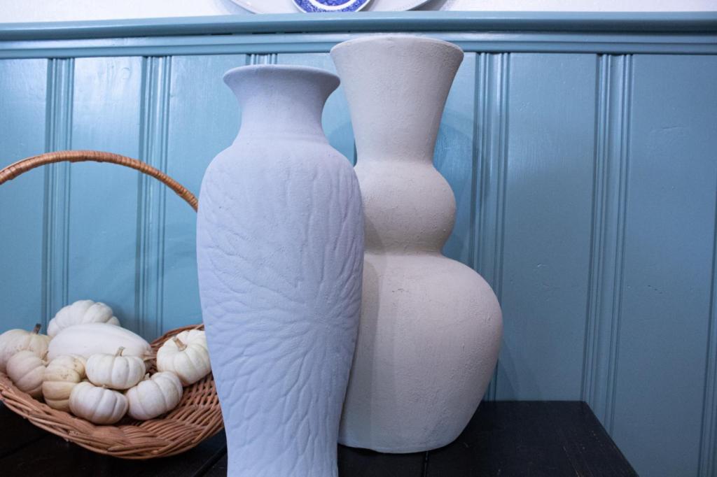 DIY textured vases are sitting on a table near a basket of mini white pumpkins with a pale blue background.